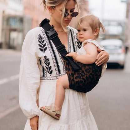 Femme portant un bébé dans un porte-bebe léopard.
