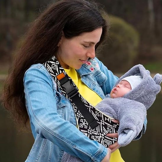 Maman portant son bébé endormi dans un porte-bébé sling