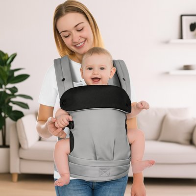Maman souriante avec bebe dans un porte-bebe gris.