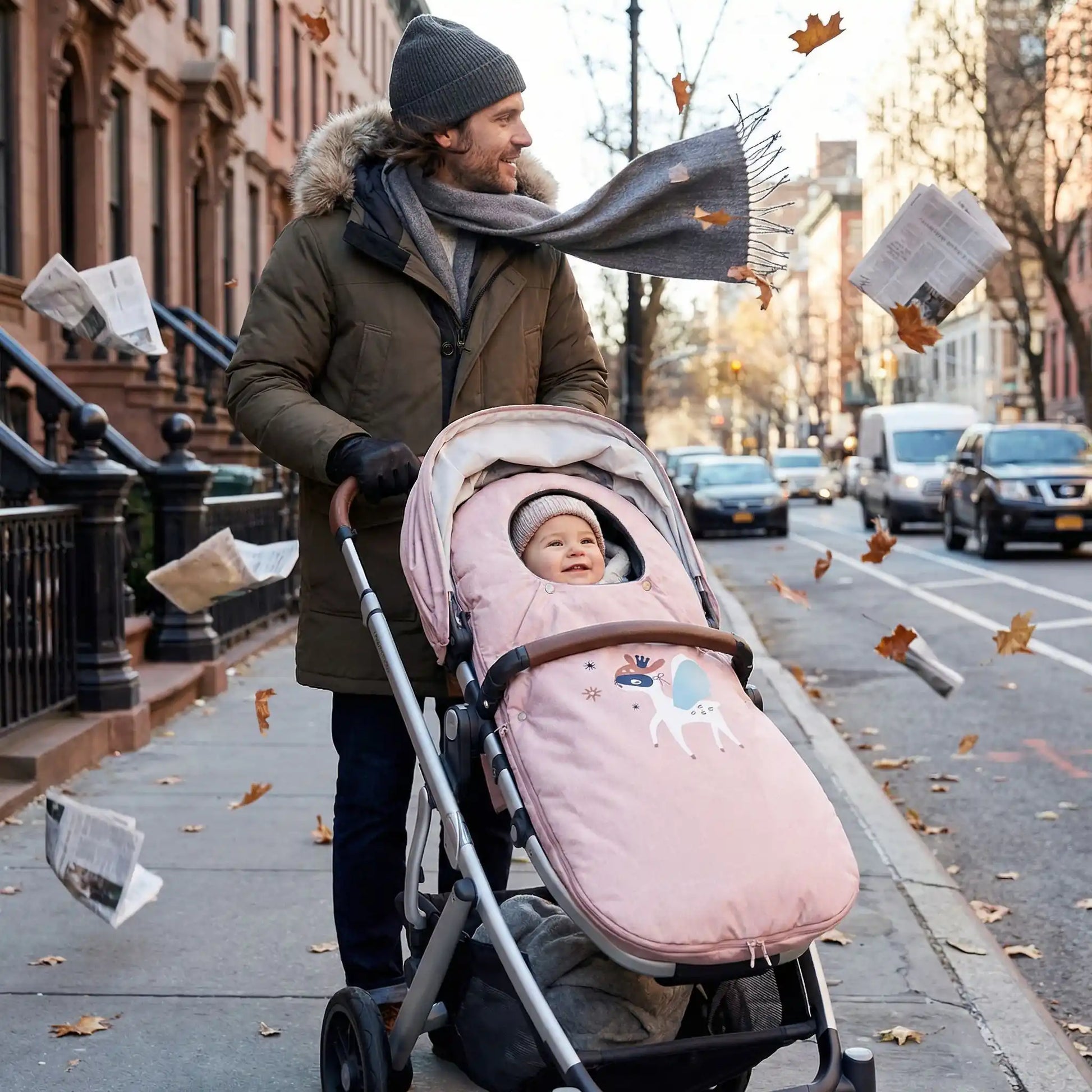 Bébé installé confortablement dans une poussette chancelière coupe-vent rose poudré, lors d’une promenade en milieu urbain par temps frais, offrant chaleur, protection et confort pendant les sorties en extérieur.
