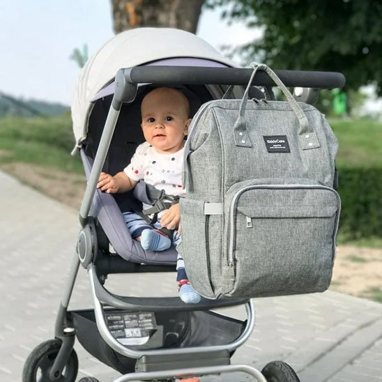 sac à dos à langer gris élégant et spacieux accroché à une poussette.